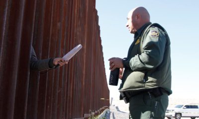 Photo of a journalist sticking her microphone through a through a border fence to interview a Border Patrol agent