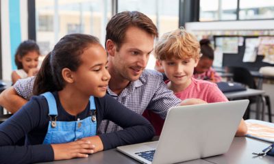 Photo of male teacher working closely with his students around a laptop