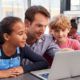 Photo of male teacher working closely with his students around a laptop